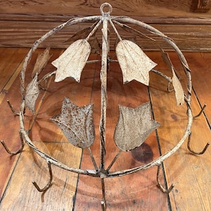 May include: A white metal pot rack with a floral design. The rack has a dome shape and features multiple hooks for hanging pots and pans.
