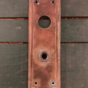 May include: A vintage brass door plate with an arched top and two keyhole openings. The plate has a worn, aged patina.