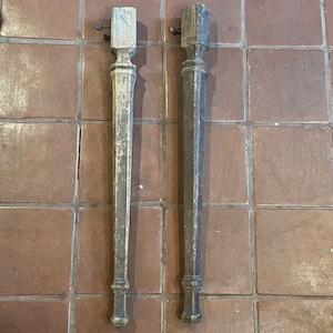 May include: Two wooden table legs with a simple turned design. The legs are weathered and have a natural wood finish.