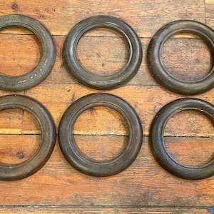 May include: Six antique wooden curtain rings with a dark brown finish are arranged on a wooden surface. The rings are circular with a thick, rounded profile, showing signs of age and wear. The wood grain is visible.