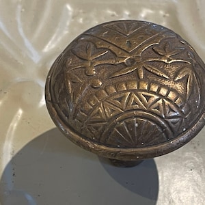 May include: A close-up of a brass door knob with an intricate geometric design. The knob is round and has a raised, textured surface.