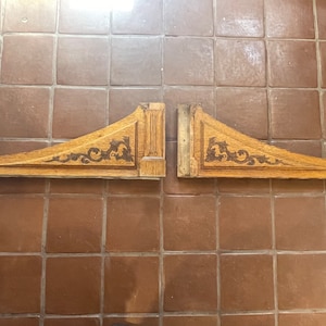 May include: Two wooden corbels with intricate carved designs. The corbels are a light brown color and have a distressed finish.