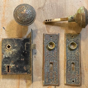 May include: Antique brass door hardware set with a round door knob, a lever handle, a door plate, and a door lock. The hardware has a decorative floral design.