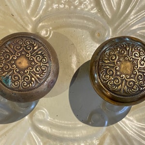 May include: Two antique brass door knobs with intricate scrollwork designs.