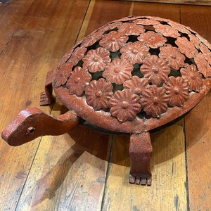 May include: A rustic metal turtle sculpture with a floral design on its shell. The turtle is painted in a reddish-brown color and has a detailed head, legs, and tail. The sculpture is likely for outdoor decor.