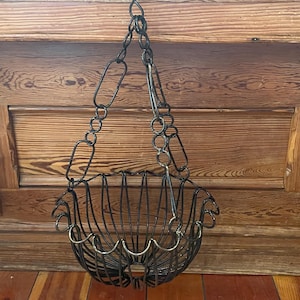 May include: A hanging wire basket constructed from dark metal with a scalloped rim and a vertical rib design. The basket is suspended by a matching dark metal chain featuring alternating oval and circular links that converge at a single top hook.