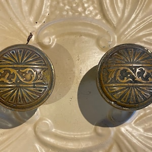 May include: Two antique brass door knobs with a sunburst design and intricate floral details.