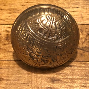 May include: A round, brass door knocker with intricate designs. The knocker features a raised, circular design with a central motif of a cross.