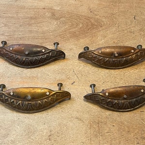 May include: Four antique brass drawer pulls with ornate designs and a leaf-like shape. Each pull has two small, round, silver-colored screws.