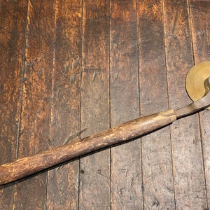 May include: A vintage wooden-handled pastry cutter with a brass blade. The blade is circular and has a spiral design. The cutter is lying on a wooden surface.