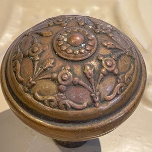 May include: A vintage brass door knob with an ornate floral design. The knob has a raised center with a circular pattern.