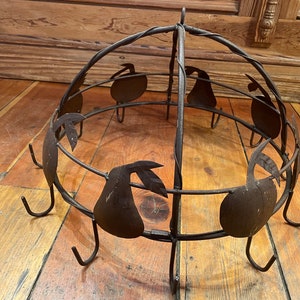 May include: A rustic metal pot rack with a pear design. The rack has a circular shape and features multiple hooks for hanging pots and pans.