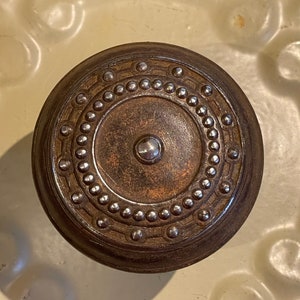 May include: A round, dark brown metal knob with a decorative design of silver studs around the edge and a smaller silver stud in the center.