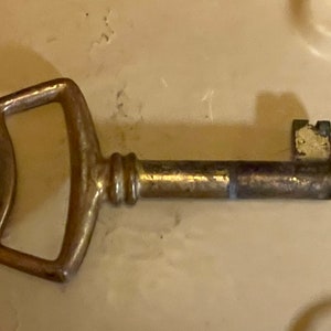 May include: A brass key with a large, rounded handle and a long, straight shaft.