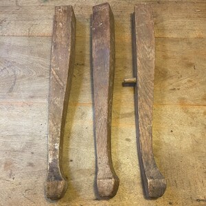 May include: Three wooden chair legs with a curved design. The legs are made of unfinished wood and have a natural brown color.