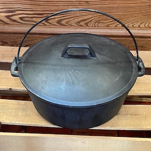 May include: Black cast iron Dutch oven with a lid and a wire handle. The pot is sitting on a wooden surface.