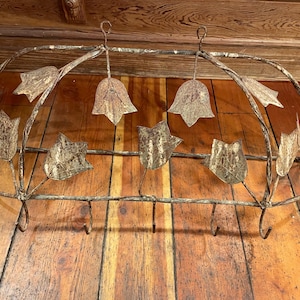 May include: Rustic metal pot rack with a decorative design of leaves and flowers. The rack has multiple hooks for hanging pots and pans.