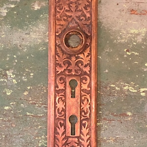 May include: Antique brass door plate with an ornate floral design and two keyholes.