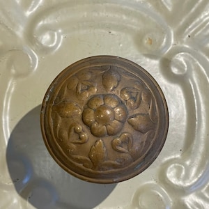 May include: A brass door knob with a floral design. The knob is round and has a raised design of flowers and leaves.