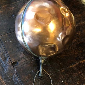 May include: A copper ball with a hammered finish and a small metal loop attached to the bottom. The ball has a shiny, metallic finish and appears to be made of solid copper.