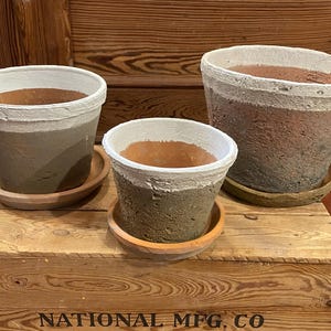 May include: Three decorative, handcrafted flower pots in varying sizes. Each pot features a two-tone design with a white rim and a textured, earthy base. The pots sit on matching saucers, perfect for indoor or outdoor plants.