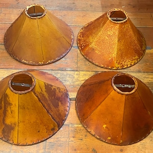 May include: Four vintage lampshades with a conical shape. The shades are made of a textured, light brown material with a darker brown trim and stitching around the edges. Each shade has a metal frame at the top.