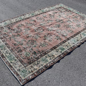 Könnte beinhalten: Ein Vintage-Teppich mit rosafarbenem Hintergrund und einem floralen Muster in Grün- und Weißtönen. Der Teppich hat einen Rand mit cremefarbenem Hintergrund und einem floralen Muster in Braun-, Grün- und Weißtönen.