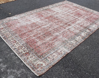 Op de afbeelding: Een vintage tapijt met een vervaagd rood en wit bloemenpatroon. Het tapijt heeft een crèmekleurige rand met een bloemenontwerp.