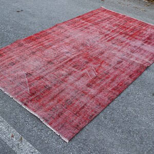 Könnte beinhalten: Ein roter Vintage-Teppich mit einem verblassten, abgenutzten Look. Der Teppich hat ein dezentes Muster und eine abgenutzte, strukturierte Oberfläche.