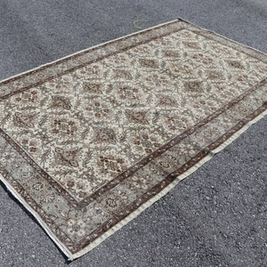 Könnte beinhalten: Ein cremefarbener Teppich mit braunem Blumenmuster. Der Teppich hat einen Rand mit einem sich wiederholenden Muster aus Braun und Creme.