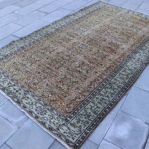 Könnte beinhalten: Ein Vintage-Teppich mit einem verblassten orangefarbenen, braunen und grünen Blumenmuster. Der Teppich hat einen hellgrünen Rand mit einem dunkelbraunen Blumendesign.