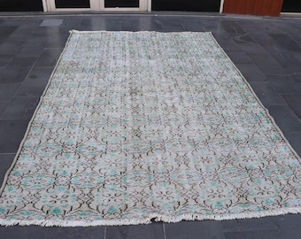 Op de afbeelding: Rechthoekig vloerkleed in vintage-stijl met een vervaagde uitstraling. Het vloerkleed heeft een lichtgrijze achtergrond met een herhalend bloemmotief in teal en bruin. De randen hebben een franje.