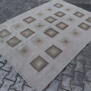 Könnte beinhalten: Ein weißer Teppich mit einem geometrischen Muster aus braunen Quadraten. Der Teppich hat einen Fransenrand.