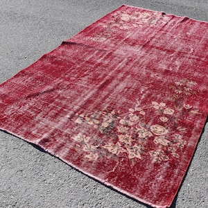 Könnte beinhalten: Ein großer, rechteckiger roter Teppich mit einem verwitterten, Vintage-Aussehen. Der Teppich weist ein Blumenmuster in Beige- und Brauntönen auf, wobei sich das Design in den Ecken und an den Rändern konzentriert. Der Teppich liegt auf einer grauen Oberfläche.