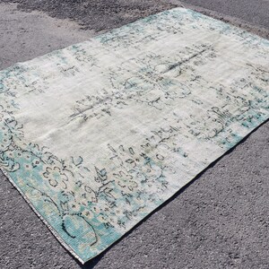 Könnte beinhalten: Ein Vintage-Teppich mit einem verblassten blauen und weißen Blumenmuster. Der Teppich hat einen abgenutzten Look und ist aus einer weichen, natürlichen Faser gefertigt.