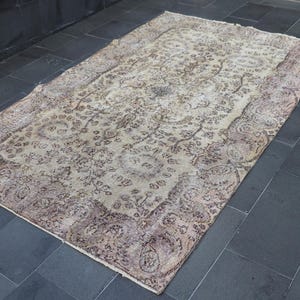 Könnte beinhalten: Ein Vintage-Teppich mit cremefarbenem Hintergrund und braunem Blumenmuster. Der Teppich hat einen abgenutzten Look und ist perfekt, um jedem Raum einen Hauch von Vintage-Charme zu verleihen.