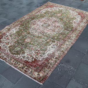 Könnte beinhalten: Ein Vintage-Teppich mit einem floralen Muster in Grün-, Rot- und Weißtönen. Der Teppich hat einen verblassten, abgenutzten Look, der ihm ein einzigartiges und antikes Aussehen verleiht.