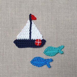Peut inclure: Un voilier en crochet avec une voile rouge et une coque bleue, ainsi que deux poissons en crochet, un turquoise et un bleu.