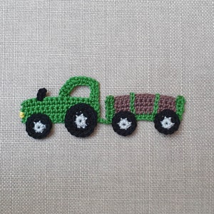 Può includere: Un camioncino giocattolo in crochet verde con un rimorchio marrone. Il camioncino ha ruote nere con centri bianchi. Il rimorchio ha ruote nere con centri bianchi.