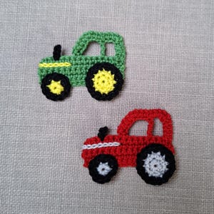 May include: Two crocheted toy tractors, one green with yellow wheels and one red with grey wheels.