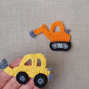 Könnte beinhalten: Zwei gehäkelte Spielzeugfahrzeuge, ein gelbes Auto und ein orangefarbenes Baufahrzeug. Beide Fahrzeuge haben graue Räder.
