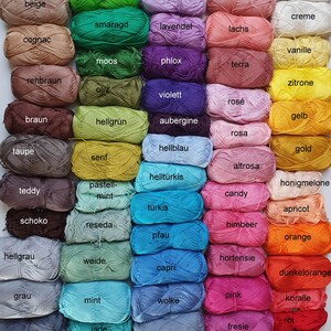 May include: A collection of colorful yarn skeins in various shades, including green, purple, pink, and blue. Each skein is labeled with its color name, such as "limone," "lavender," and "pink." The yarn is arranged in neat rows, showcasing a wide range of hues.
