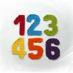 May include: A collection of six colorful, crocheted numbers: 1 in red, 2 in blue, 3 in green, 4 in yellow, 5 in orange, and 6 in purple. These handmade numbers are likely used for educational purposes or as decorative elements.