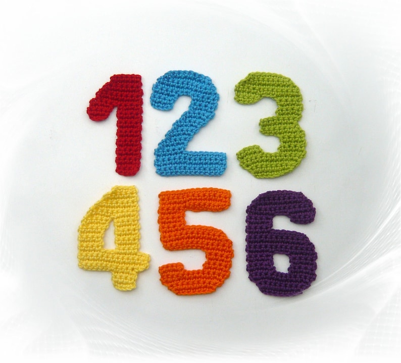 May include: A collection of six colorful, crocheted numbers: 1 in red, 2 in blue, 3 in green, 4 in yellow, 5 in orange, and 6 in purple. These handmade numbers are likely used for educational purposes or as decorative elements.