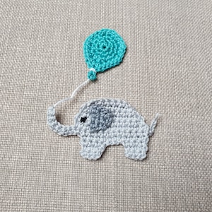 Könnte beinhalten: Ein grauer gehäkelter Elefant, der einen türkisfarbenen gehäkelten Ballon hält. Der Elefant hat ein kleines schwarzes Auge und ein graues gehäkeltes Ohr.