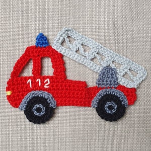 Könnte beinhalten: Gehäkelter Feuerwehr-Applikation in Rot, mit blauem Dachlicht und grauer Leiter. Die Räder sind schwarz und grau, und der Truck hat die Nummer 112 in Weiß. Ideal für Bastelarbeiten und Verzierungen.