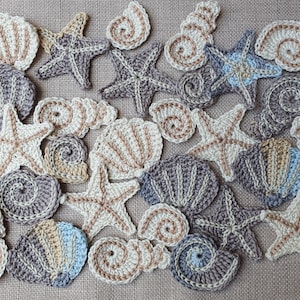 Könnte beinhalten: Eine Sammlung gehäkelter Muscheln und Seesterne in verschiedenen Brauntönen, Beige und Blau. Die gehäkelten Gegenstände sind auf einem strukturierten Stoffhintergrund angeordnet.