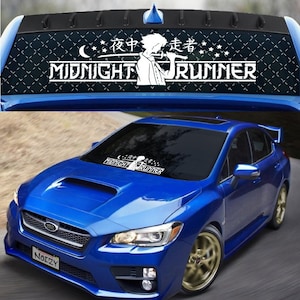 May include: A blue Subaru car with a white vinyl decal on the windshield that says "Midnight Runner" with a cartoon character holding a microphone. The decal also includes the Japanese characters for "Midnight Runner".