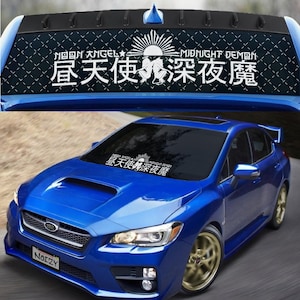 May include: A blue Subaru WRX with a black windshield banner that reads "昼天使深夜魔" in white text. The banner also includes the text "N回图 大NGEL" and "MIDNIGHT DEMON" in white text. The car has a black license plate that reads "NOIZY".