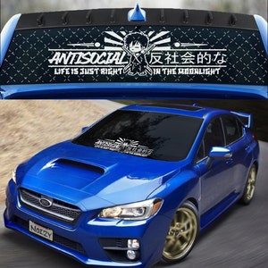 May include: A blue Subaru Impreza with a black and white windshield sunshade featuring an anime character and the text "ANTISOCIAL、反社会的な LIFE IS JUST RIGHT IN THE MOONLIGHT".
